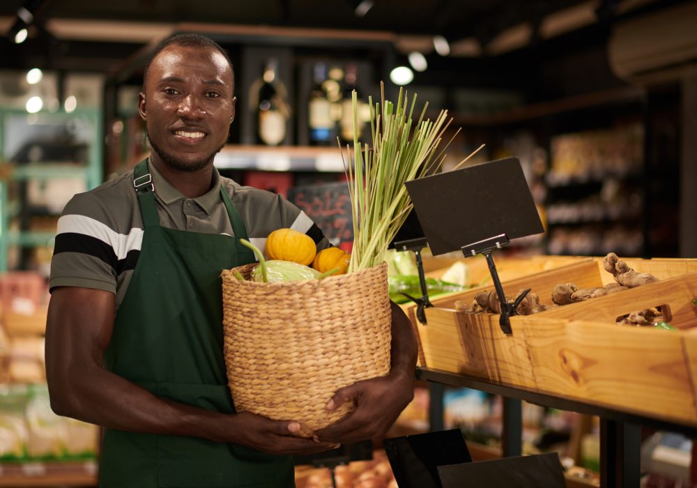 Portrait of smiling grocery store worker with basket of fresh fruits and vegetables