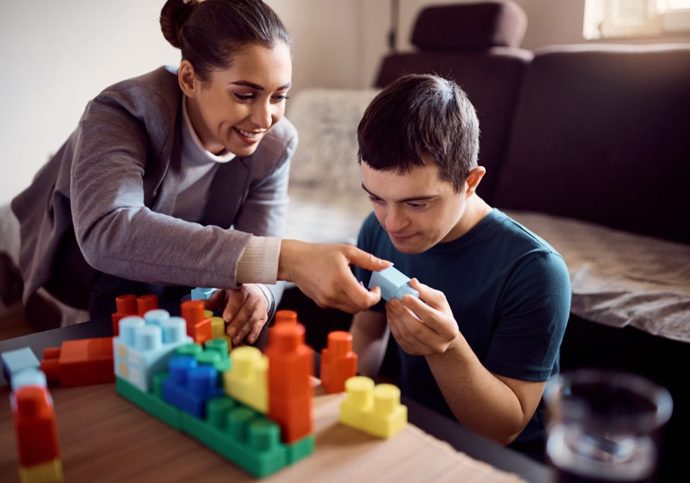 Happy psychologist and man who has down syndrome playing with toy blocks during home visit.